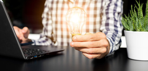 Successful business idea and creative innovation concept, close up business man holding lighting bulb and tablet with financial graph on table