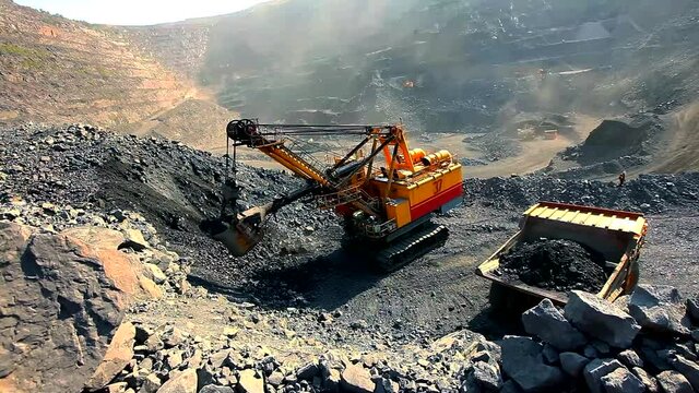An excavator pours soil into a dump truck in a quarry. Iron ore mining in an open pit. Equipment for the extraction of iron ore in a quarry