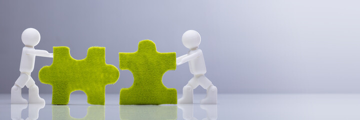 Two Miniature Human Figures Solving Green Jigsaw Puzzles