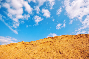 Large pile of industrial sand, stockpiled and prepared for use in construction and road construction, against a blue sky