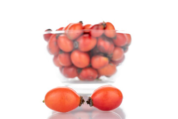 Several bright red ripe wild rose berries in a glass dish, close-up, isolated on white.