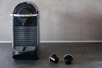 Espresso pod machine and capsules on home kitchen table, front view.