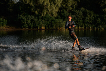 Fototapeta na wymiar Active sportive man in wetsuit energetically balancing on water surface on wakeboard