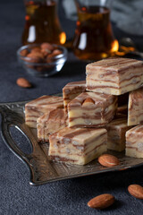 Delicious slices of Oriental milk halva with almonds and cocoa on dark gray background. Uzbek traditional handmade sweets. Vertical format