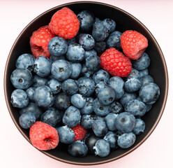 Blueberries mixed with raspberries in a cup, top view.