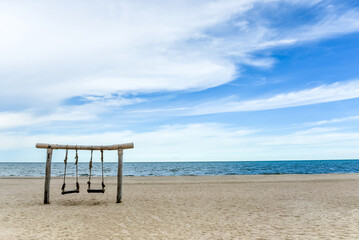 Wooden swing on the beach with sea, sand, cloud and blue sky of tropical island banner background and copy space