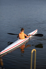 The boy is kayaking. In a yellow vest.