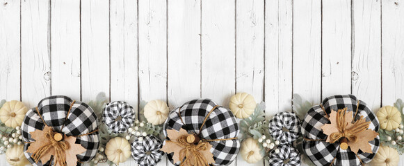 Modern farmhouse autumn bottom border over a white wood banner background. Black and white buffalo plaid pumpkins, leaves and berries. Top down view with copy space.