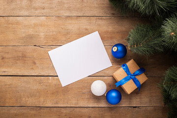 Blank sheet of paper and a gift under the Christmas tree on a wooden background. Top view, flat lay