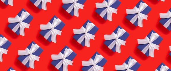 Obraz premium Lots of Christmas gift boxes blue with a white ribbon on a red background. Top view, flat lay. Banner