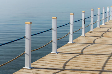 Fototapeta premium Travel. Pier on the sea. View at the sea from the wooden pier with posts and ropes with sparkling sea water