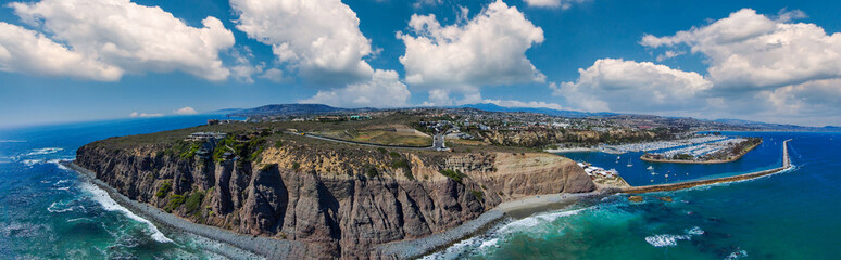 a stunning aerial panoramic shot of the deep blue ocean water and the sandy beach and the boats on the harbor with beach front homes and blue sky and clouds in Dana Point California - obrazy, fototapety, plakaty