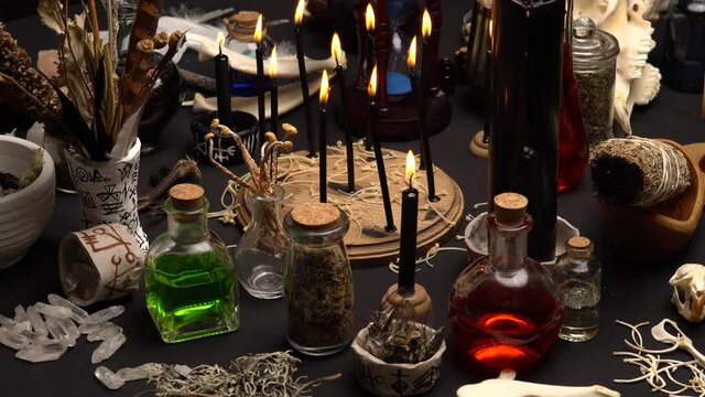 Witchy table arranged with witch craft magic items. Magic mushrooms. Still life with black magic candles, ritual dry weeds, animals bones and green potion vial. Halloween concept.