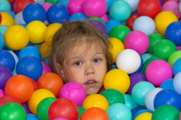 Fototapeta na wymiar Head of sad caucasian little girl of five years old among multicolor balls in play center