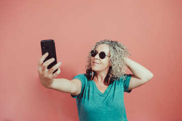 middle-aged blonde woman in sunglasses takes a selfie while touching her hair