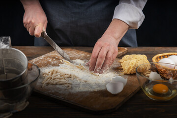 Women's hands, flour and dough. A woman in an apron cooking dough for homemade baking, a rustic home cozy atmosphere, a dark background with unusual lighting.