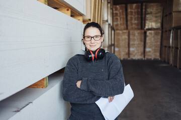 Smiling woman with ear muffs in a warehouse or factory - obrazy, fototapety, plakaty