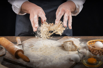 Women's hands, flour and dough. A woman in an apron cooking dough for homemade baking, a rustic home cozy atmosphere, a dark background with unusual lighting.