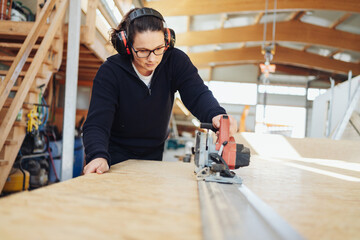Female carpenter or joiner at work in a woodworking factory - obrazy, fototapety, plakaty