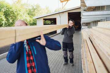 Two colleagues carrying a large beam of wood at a factory