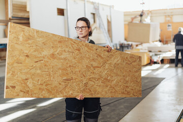 Female worker carrying a sheet of plywood or compressed board