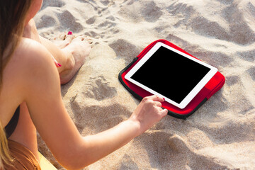 Young sporty woman using tablet on the beach to watch fitness courses. Wireless communication and Internet for active lifestyle, yoga and exercising