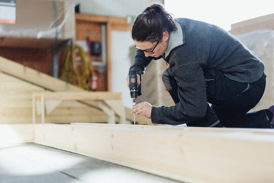 Female carpenter or joiner kneeling down drilling a hole