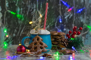 Fototapeta na wymiar Christmas garland, delicious cocoa with chewing marshmallows in a beautiful cup with a straw, sweet gingerbread cookies, star anise, cinnamon sticks and New Year's decor on the table.