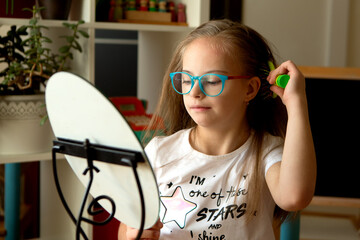 A beautiful girl with Down syndrome combs in front of a mirror