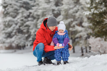 Smiling little girl having fun with father in winter park. Cute two year old kid with parent playing snowballs maker toy. Concept of happy family and childhood, togetherness, care, winter games
