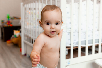 a 12-month-old baby is standing by his crib. portrait of a child. children.