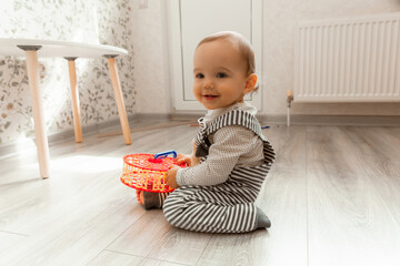 cute smiling baby 12 months old sits on the floor in his room and plays with toys.