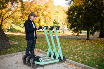 Transportation ecology. Green sustainable mobility Young man unlocks an e-scooter with his mobile phone. Electric scooter new way city. Green transportation. Sustainable climate neutral cities goals.