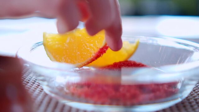 Hand covering orange slice with chili powder on glass plate