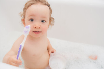 Funny happy baby with curly hair taking bath and brushing her teeth. A cute baby girl is happy in the bathroom - 460528940