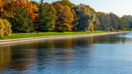 View of river and autumn park. Trees with yellow and red leaves reflecting in water. High quality photo