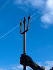 Poseidon's trident against a blue sky and a flying plane