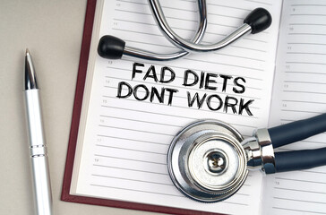 On the table is a stethoscope, a pen and a notebook in which it is written - Fad Diets Dont Work