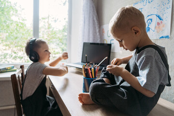 Two boy schoolkids brothers wearing headphones sitting near laptop at home. Back to school, Homeschooling, online study, home quarantine online learning education.