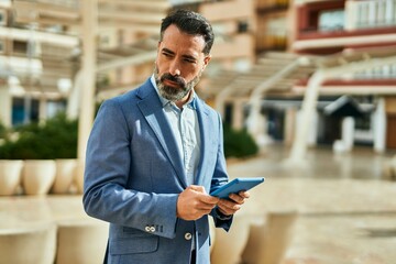 Middle age businessman with serious expression using touchpad at the city.