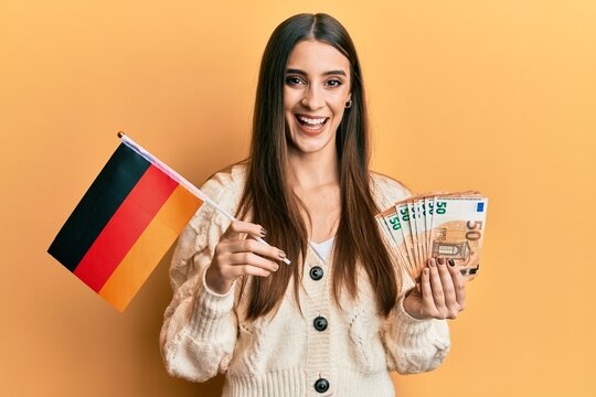 Beautiful brunette young woman holding germany flag and euros banknotes smiling and laughing hard out loud because funny crazy joke.