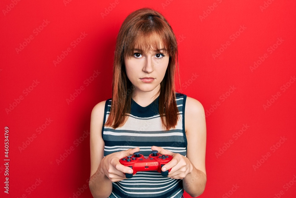 Poster redhead young woman playing video game holding controller relaxed with serious expression on face. s