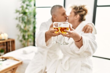 Senior caucasian couple kissing and toasting with champagne sitting on massage table at beauty center.