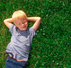 Little beautiful kid outdoor. Lay on green grass.