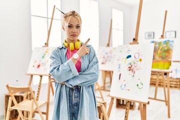 Naklejka premium Young caucasian girl at art studio pointing with hand finger to the side showing advertisement, serious and calm face