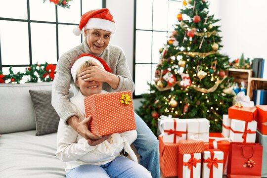 Senior man suprising his wife with christmas gift at home.