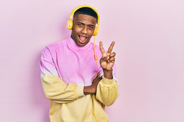 Young black man listening to music wearing headphones smiling with happy face winking at the camera...