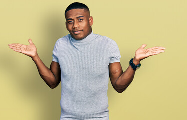 Young black man wearing casual t shirt clueless and confused expression with arms and hands raised....