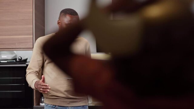 Black man having video call on laptop from home at coronavirus outbreak while playful daughter running around in viking helmet with sword and screaming. Businessman finishing talk due to noisy kid