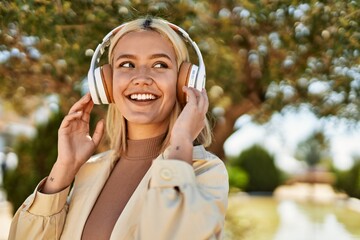 Young blonde girl smiling happy using headphones at the city.